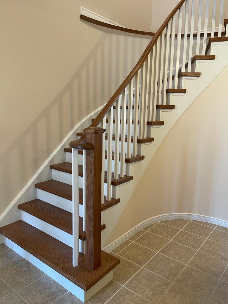 Curved spiral stair capping remodeling project with oak wood and white spindles in Mississauga